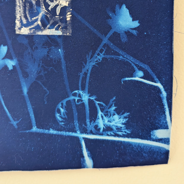 Wall hanging on a piece of driftwood of a blue cyanotype on fabric. Flowers and seaweed are imprinted.