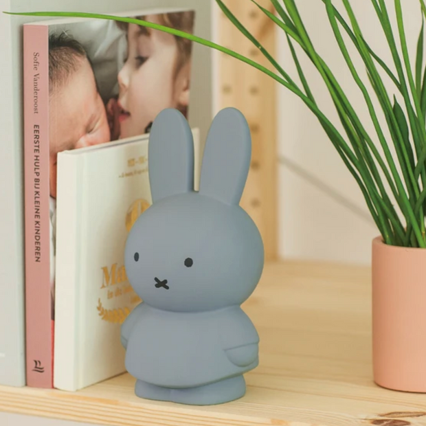 Miffy shaped coin bank, completely colored a silver shade of blue with gray eyes and mouth. She stands wearing a dress with her arms at her sides.