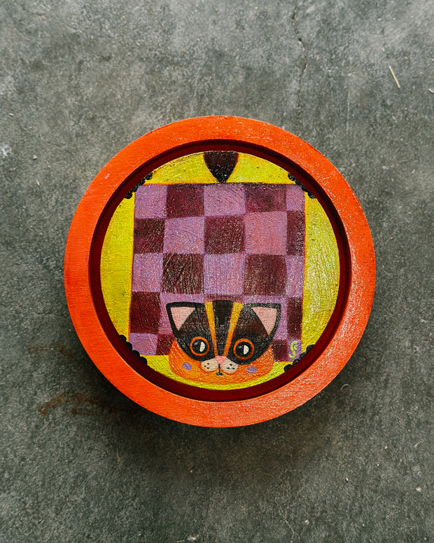 Painting on rounded inlayed wood panel of a flying squirrel, with a purple checkerboard pattern and an orange face. Background is yellow and border is orange.