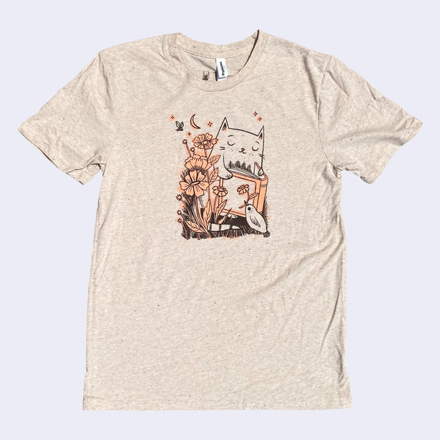 Tan t-shirt with an illustration of a cat reading a book with flowers and a small bird holding a flower in its beak.