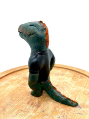 Sculpture of a dark bluish green dinosaur with a simple cartoon face and a wide closed mouth smile and a t-shirt that reads "T-Rex" in red.