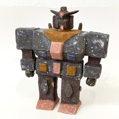 Ceramic sculpture of a Gundam with a wide, blocky body and several buttons and suit detailing with a pointed helmet.