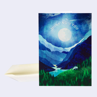 Greeting card with an illustrated scene on the front of a large moon glowing over a river and green forest and tall blue mountains. Text reads "Thinking of You" wrapped around the moon.