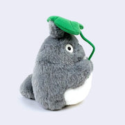 Plush doll of Totoro holding a large green leaf in front of its face and overhead. 