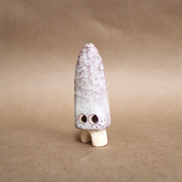 Small whittled wooden sculpture of a long pointed mushroom, painted white with small cartoon eyes and freckles. It has very short legs and looks off to the side.
