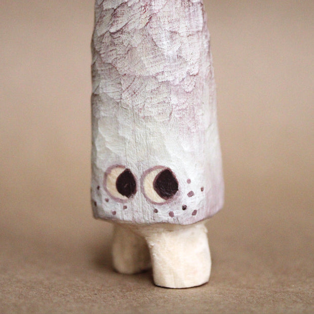 Small whittled wooden sculpture of a long pointed mushroom, painted white with small cartoon eyes and freckles. It has very short legs and looks off to the side.