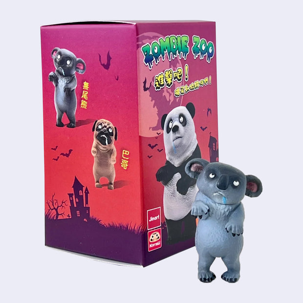 Vinyl figure of a zombie koala, standing on its hind legs with drool coming out of its mouth and its eyes rolled up. It stands next to its product packaging.