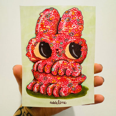 Illustration on light green paper of a cute cartoon bunny with very large eyes and a tiny nose and smile. Its body is made up of pink and red doodles of flowers, mushrooms and skulls. The bunny stands on its hind legs and looks up and to the side.