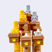 6 retractable pens with cats inside of cardboard boxes as the pen toppers. Cats are either gray on gray pens, calico on brown pens, or orange on orange pen bodies.