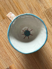 Overhead view of cream colored ceramic mug with a blue sunshine or starburst illustration inside.