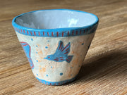 Ceramic mug, mostly cream colored with a blue rim and design of a blue hummingbird on the side