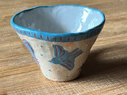 Ceramic mug, mostly cream colored with a blue rim and design of a blue bird with red lines on the side of the mug.