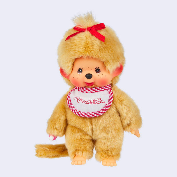 Plush doll of Monchhichi, a cute monkey that has a baby animal face with rosy cheeks and brown eyes. It has beige fluffy fur, wears a white and red plaid bib, red hair bow, and has a pacifier in its hand that can go in its mouth.