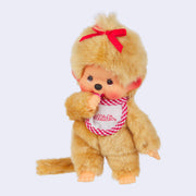 Plush doll of Monchhichi, a cute monkey that has a baby animal face with rosy cheeks and brown eyes. It has beige fluffy fur, wears a white and red plaid bib, red hair bow, and has a pacifier in its hand that can go in its mouth.