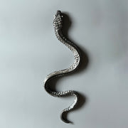 Ceramic sculpture of a snake, with a long dark silver body and silver eyes. It is seen from overhead, slithering forward.