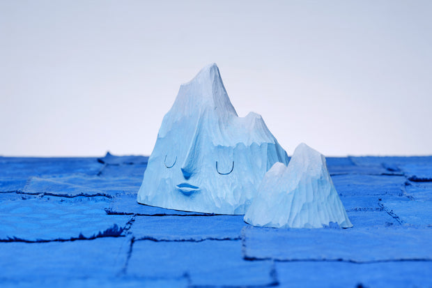 Set of 2 carved wooden sculptures, painting blue, of mountain ranges. One has a closed eye, calm facial expression and the other is without a face and smaller in size.