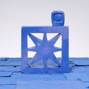 Carved wooden sculpture made to look like a cement breeze block with a centralized star pattern. The block is entirely purplish blue and a small TV sits on top of it.