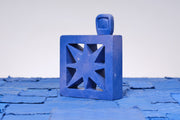 Carved wooden sculpture made to look like a cement breeze block with a centralized star pattern. The block is entirely purplish blue and a small TV sits on top of it.