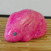 Sculpture of a bright pink bunny with blue eyes. It sits huddled into itself, without any limbs exposed.