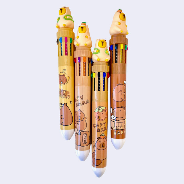 4 pens with 10 color options. Each pen is topped with a rubber capybara figure, 2 of them are wearing a turtle shaped backpack and the other 2 have a citrus atop their head.