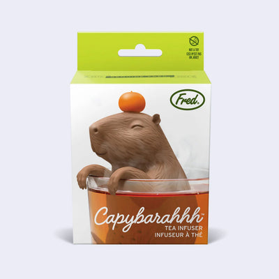 Product packaging for a capybara shaped silicone tea infuser, sitting inside of a brewing cup of tea with a silicone orange atop its head.