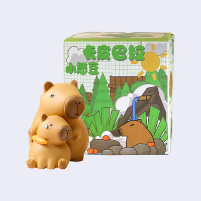 Vinyl figure of 2 capybaras, one sits on the ground with a nervous sweat bead on its forehead and another stands behind it holding a carrot to the other's neck.