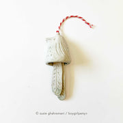 Off white ceramic bell with the top made to look like a bird and the bell part 2 feathers. Attached to the top is a red and white twine.