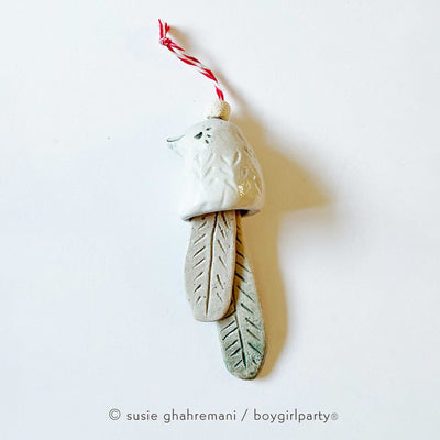 Off white ceramic bell with the top made to look like a bird and the bell part 2 feathers. Attached to the top is a red and white twine.