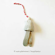 Off white ceramic bell with the top made to look like a bird and the bell part 2 feathers. Attached to the top is a red and white twine.