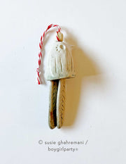 Off white ceramic bell with the top made to look like a bird and the bell part 2 feathers. Attached to the top is a red and white twine.