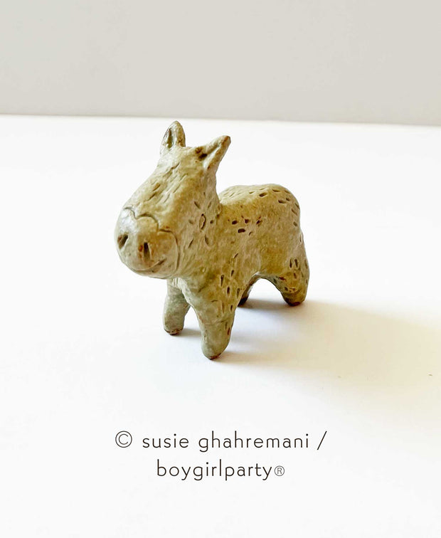 Brown toned ceramic sculpture of a small donkey with line pattern around its eye, pointed ears, rounded snout and small legs.