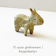 Brown toned ceramic sculpture of a small donkey with line pattern around its eye, pointed ears, rounded snout and small legs.