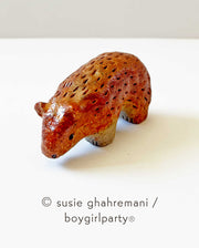 Small ceramic sculpture of a copper brown bear with simplistic body and head features, looking down.