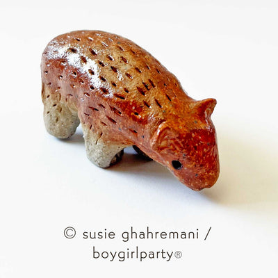 Small ceramic sculpture of a copper brown bear with simplistic body and head features, looking down.