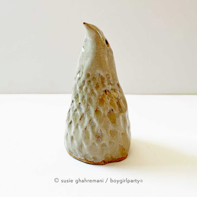 Ceramic sculpture of a bird, with a pointed cone shaped body. It has textured feathers and a pointed beak that looks upward.