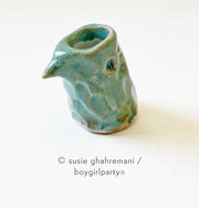 Small teal ceramic bird head with an opening for ink.