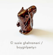 Small brown ceramic sculpture of a squirrel with a large tail.