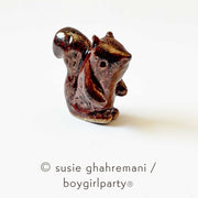 Small brown ceramic sculpture of a squirrel with a large tail.