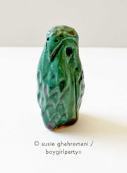 Small ceramic sculpture of a turquoise colored owl, standing with simplistic features and carved out feathers.