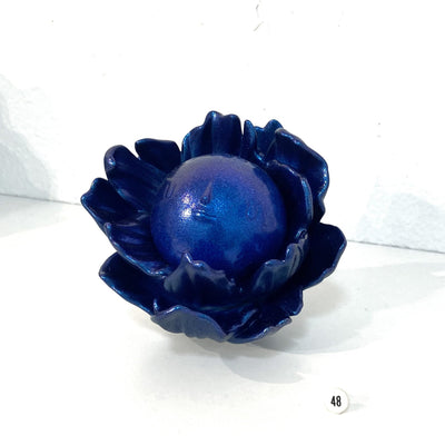 Very dark blue, glittery vinyl sculpture of a round full moon with a small minimalistic face. It sits within a series of flower petals, as if it is the pistil of the flower.