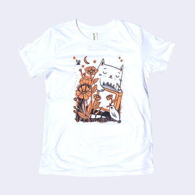 White children's t-shirt with an illustration of a cat reading a book with flowers and a small bird holding a flower in its beak.