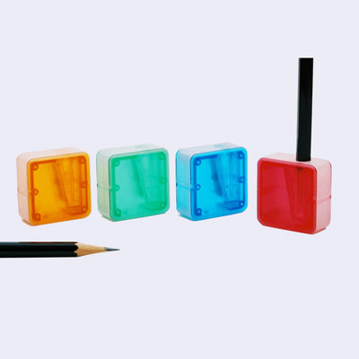 4 square shaped pencil sharpeners: clear orange, clear green, clear blue and clear red.