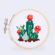 Cross stitch embroidery in a bamboo circle of a set of cacti plants, green with red and orange blossoms.