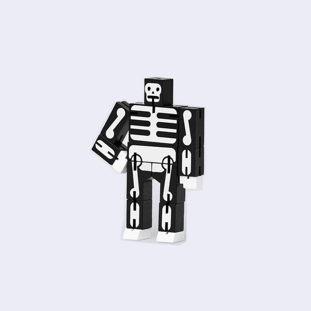 Wooden robot made out of many rectangular parts standing with its arms on its hips. Toy is painted black with white bone detailing.