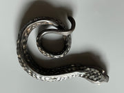 Ceramic sculpture of a dark silver snake with silver colored eyes and imprinted scales along its body. Its tail is curled into itself.