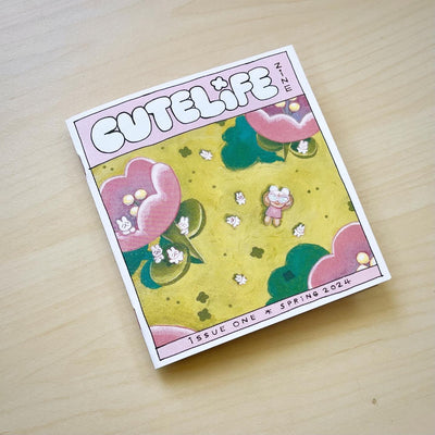 "Cutelife" zine cover, featuring an illustration of a small girl laying in an open green field, seen from overhead. Many small bunnies are around her and large pink flowers.