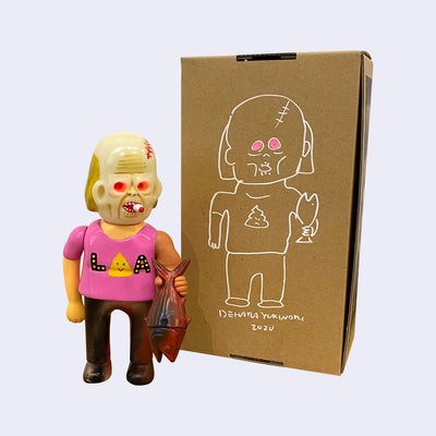 Vinyl figure of a man with a zombie like face- hollowed out pink eyes, a forehead scar and smoking a thick cigarette. He holds a bonito fish and wears a pink shirt that says "LA" with a smiling yellow poop emoji. It stands next to a cardboard box with a line art illustration of himself on it.