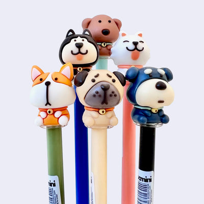 Set of 6 gel pens with different cartoon dogs as the pen toppers, each with an exaggerated, large head. Dogs are: corgi, pug, schnauzer, husky, chocolate lab and samoyed.