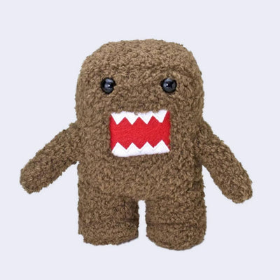 Fluffy plush doll of Domo, with brown fur, an inlayed embroidered red mouth with jagged white teeth and black beads for eyes. It stands with its arms out to its side.