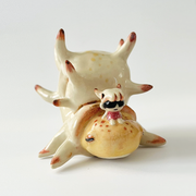 Ceramic sculpture of a cream colored shelled bug or crustacean, akin to a snail with a spiked and rounded shell. A small character sits atop its head.